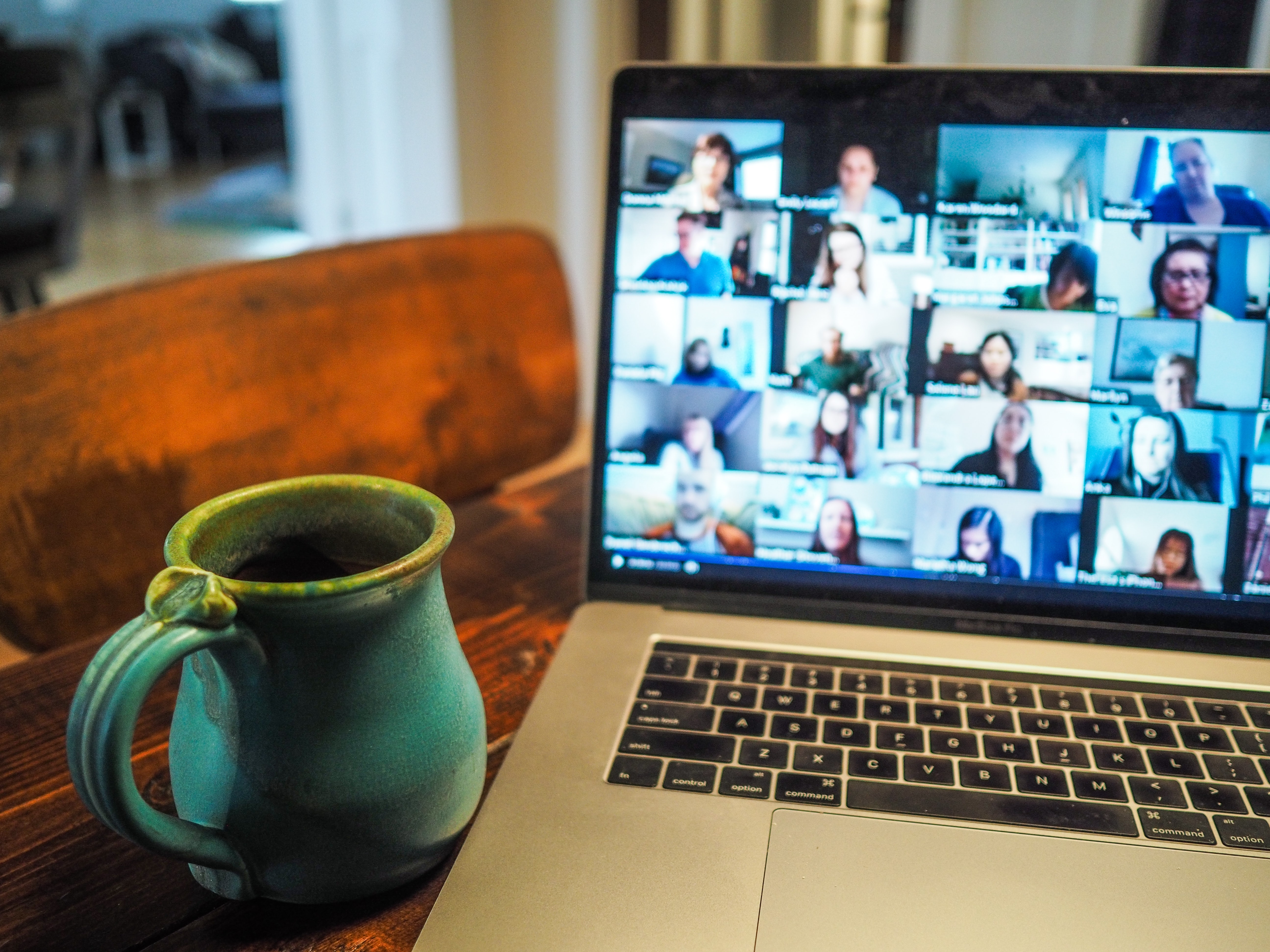 A laptop showing a zoom call with lots of people and a cup of tea on a table