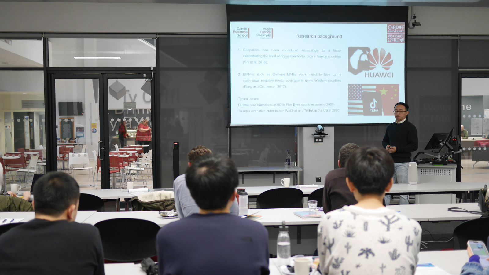 A man presenting to a class stood in front of a large screen
