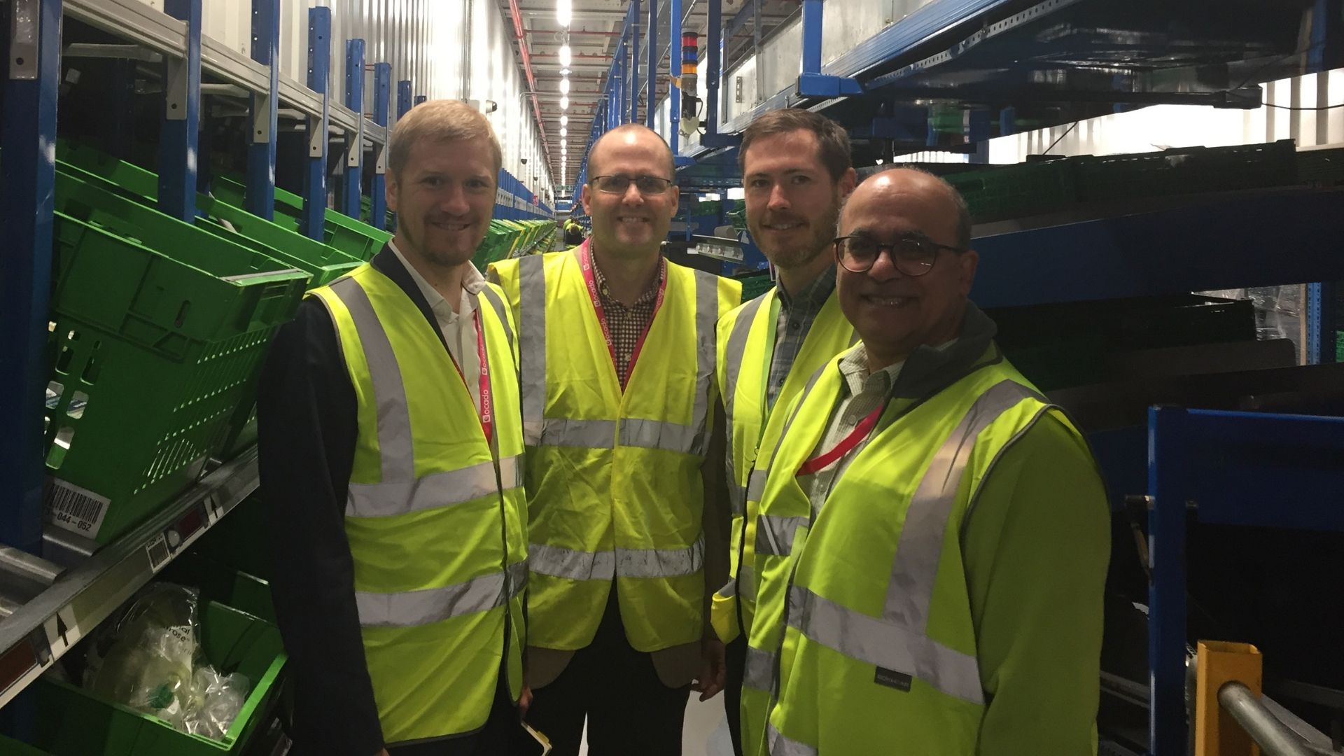 Four men wearing high-visibility jackets in a warehouse