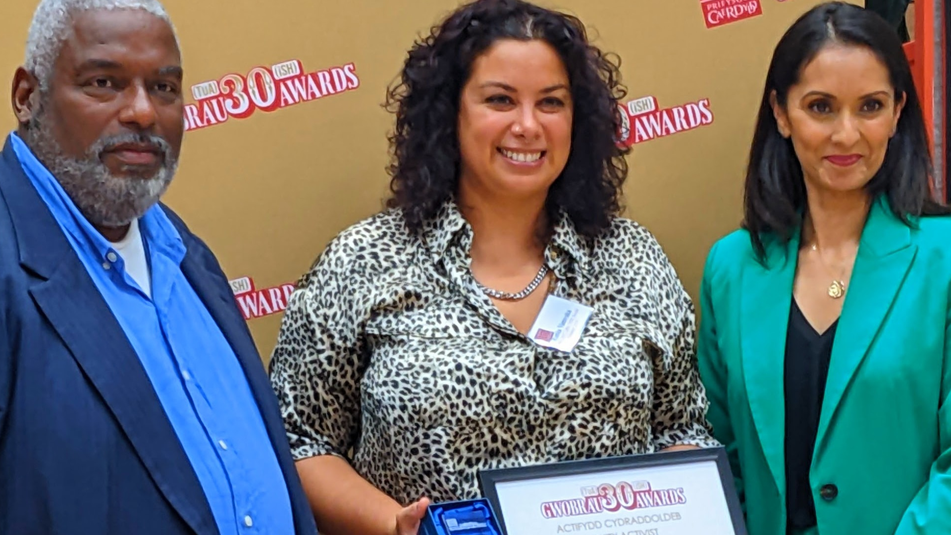 Two people presenting an award to another person who's holding a certificate