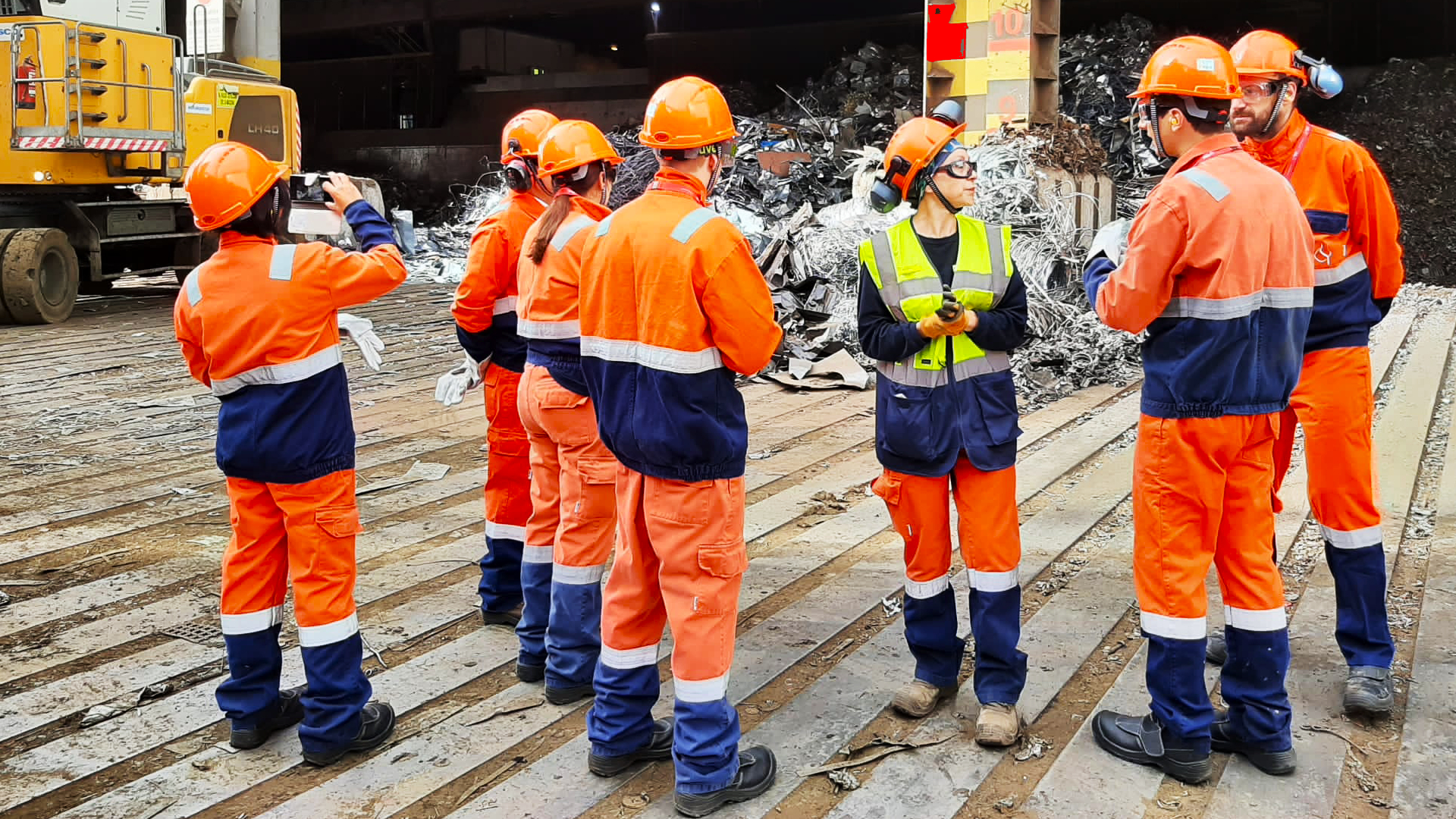 A group of people on high vis clothing at a scrap repository.
