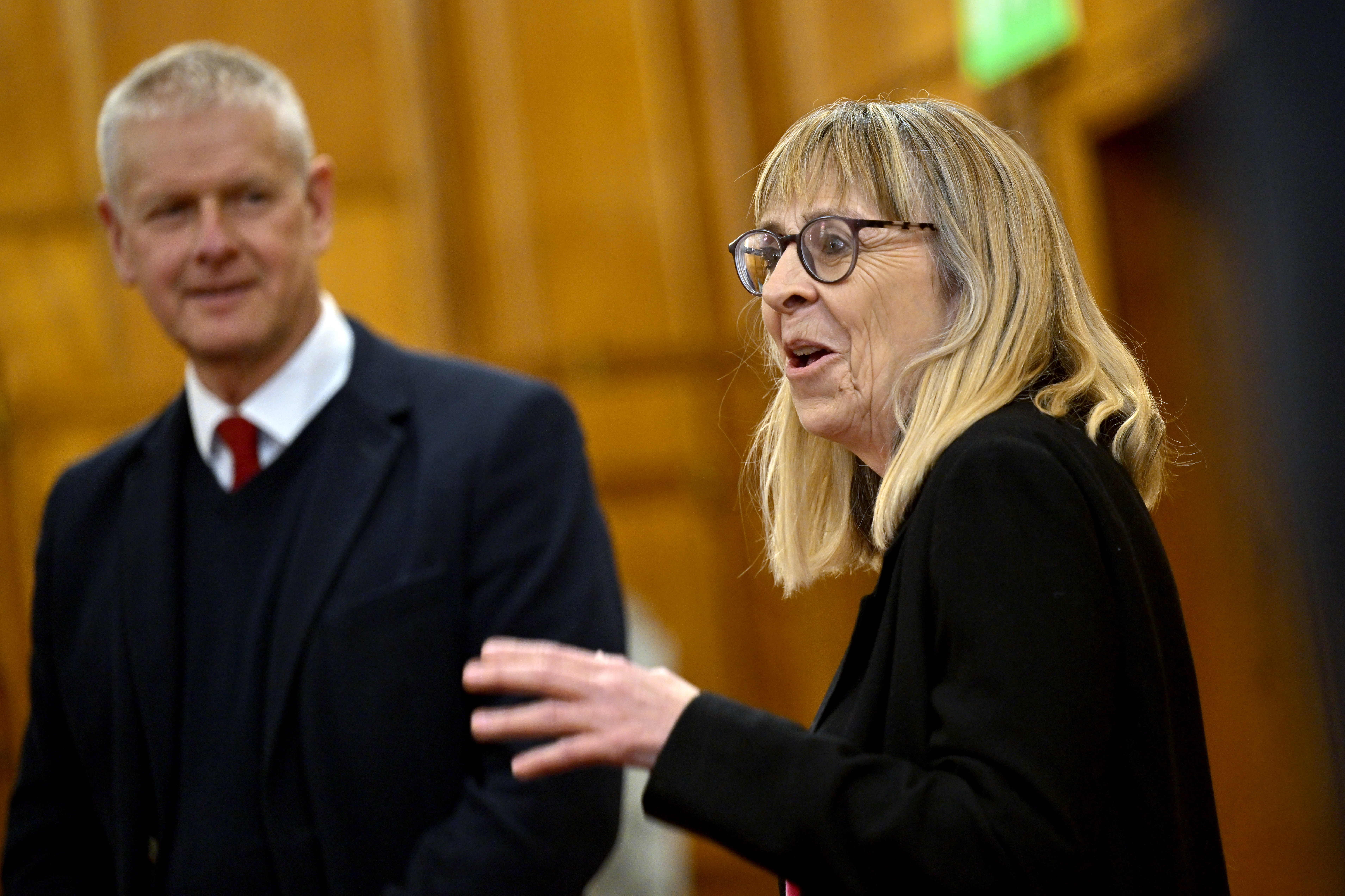 A woman talks while a man behind her looks on